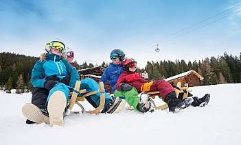Familie beim Rodeln im Schnee Vier Personen in Skikleidung sitzen auf Schlitten im Schnee.