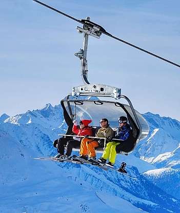 Skiers on a chairlift Four skiers riding a chairlift above snowy mountains.
