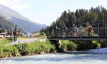 Horse and cyclists near river A horse rider and cyclists crossing a bridge by a river.
