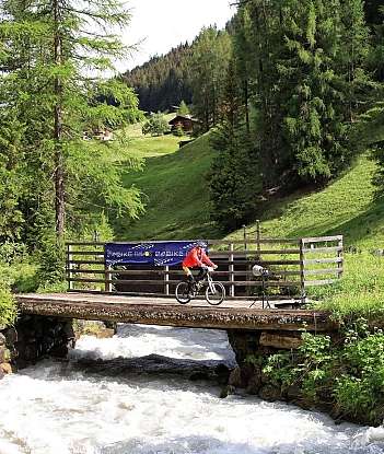 Cyclist on a wooden bridge A cyclist crosses a bridge over a rushing river in a green landscape.