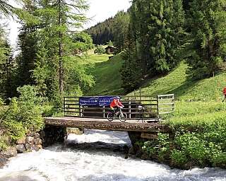 Cyclist on a wooden bridge A cyclist crosses a bridge over a rushing river in a green landscape.