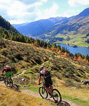Mountain Biking in Scenic Landscape Two cyclists riding on a trail with mountains and a lake in the background.