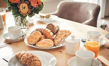 Frühstückstisch mit Gebäck Ein gedeckter Tisch mit verschiedenen Brötchen und Blumen.